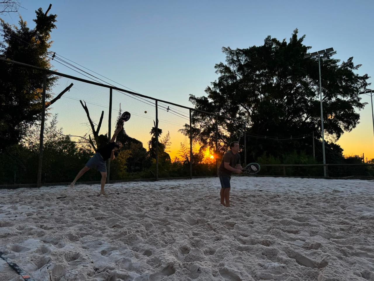 Adultos jogando beach tennis ao entardecer